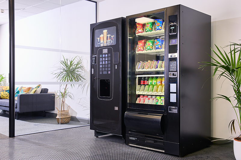 A large coffee dispensing machine and vending machine with P66 card readers in an office break room.