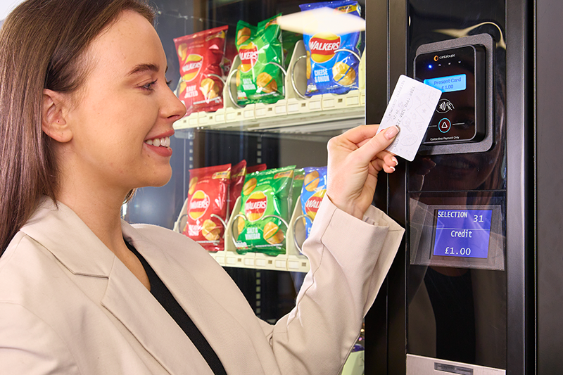 A woman taps to pay with a credit card at a vending machine.