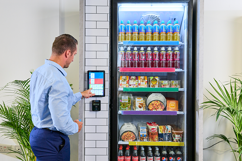 A man stands in front of a cooler cafe tapping the touchscreen to the left of the machine.