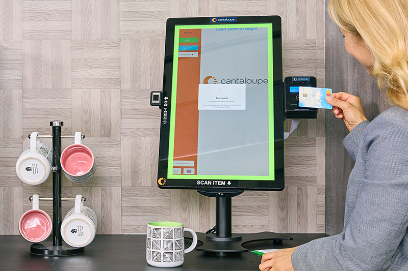 A woman pays with a credit card by tapping it on the card reader attached to a large touchscreen kiosk.