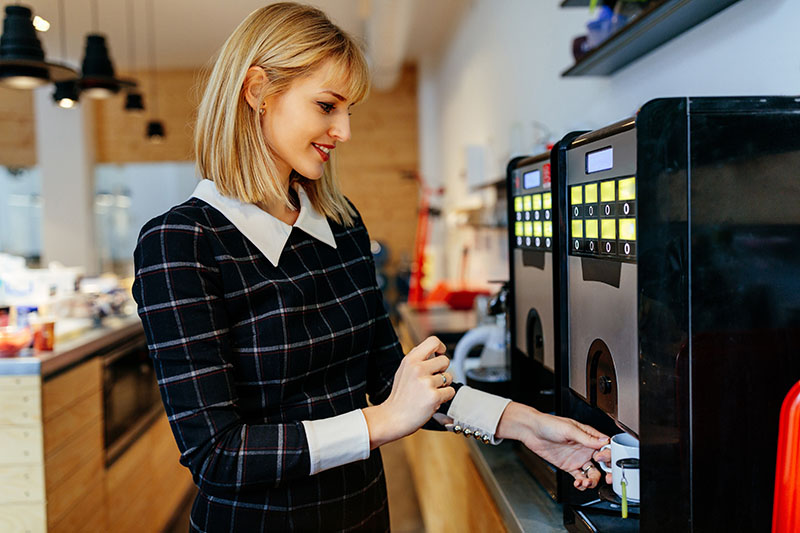 A young women gets a coffee at an office coffee machine.